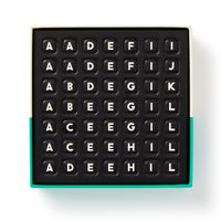 The Scrumble Magnetic Fridge Game by Brass Monkey features black letter tiles with capital letters arranged in rows, similar to crossword magnets, all in a box with a green-edged bottom.