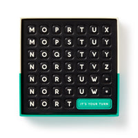 The Brass Monkey Scrumble Magnetic Fridge Game features a black 7x7 crossword-style game board with lettered tiles and a green ITS YOUR TURN tile in the bottom right, all placed in an open box with a green edge.