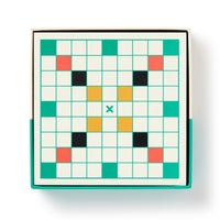 The Brass Monkey Scrumble Magnetic Fridge Game features a square, crossword-style grid of white squares with clusters of red, black, and yellow squares plus a green X near the center, bordered in green and housed in a box.