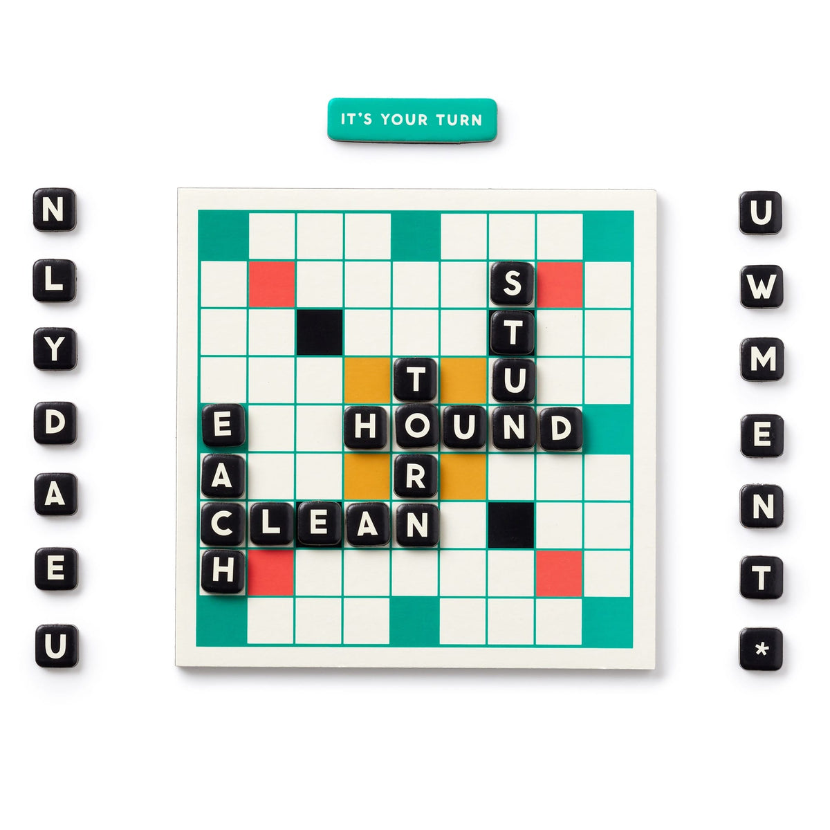 The Brass Monkey Scrumble Magnetic Fridge Game features words like HOUND, TURN, STUN, EACH, and CLEAN on a board with scattered tiles and a teal piece reading “IT’S YOUR TURN” at the top.