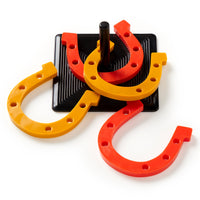 Brass Monkey’s Giddy Up Tabletop Horseshoes Game features two yellow and two orange rubber horseshoes surrounding a black peg on a square black base, making it an ideal party game for indoor fun.