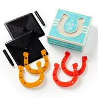 The Brass Monkey Giddy Up Tabletop Horseshoes Game includes two black bases, two black pegs, orange and red rubber horseshoes, and comes in a blue box—perfect for party fun.