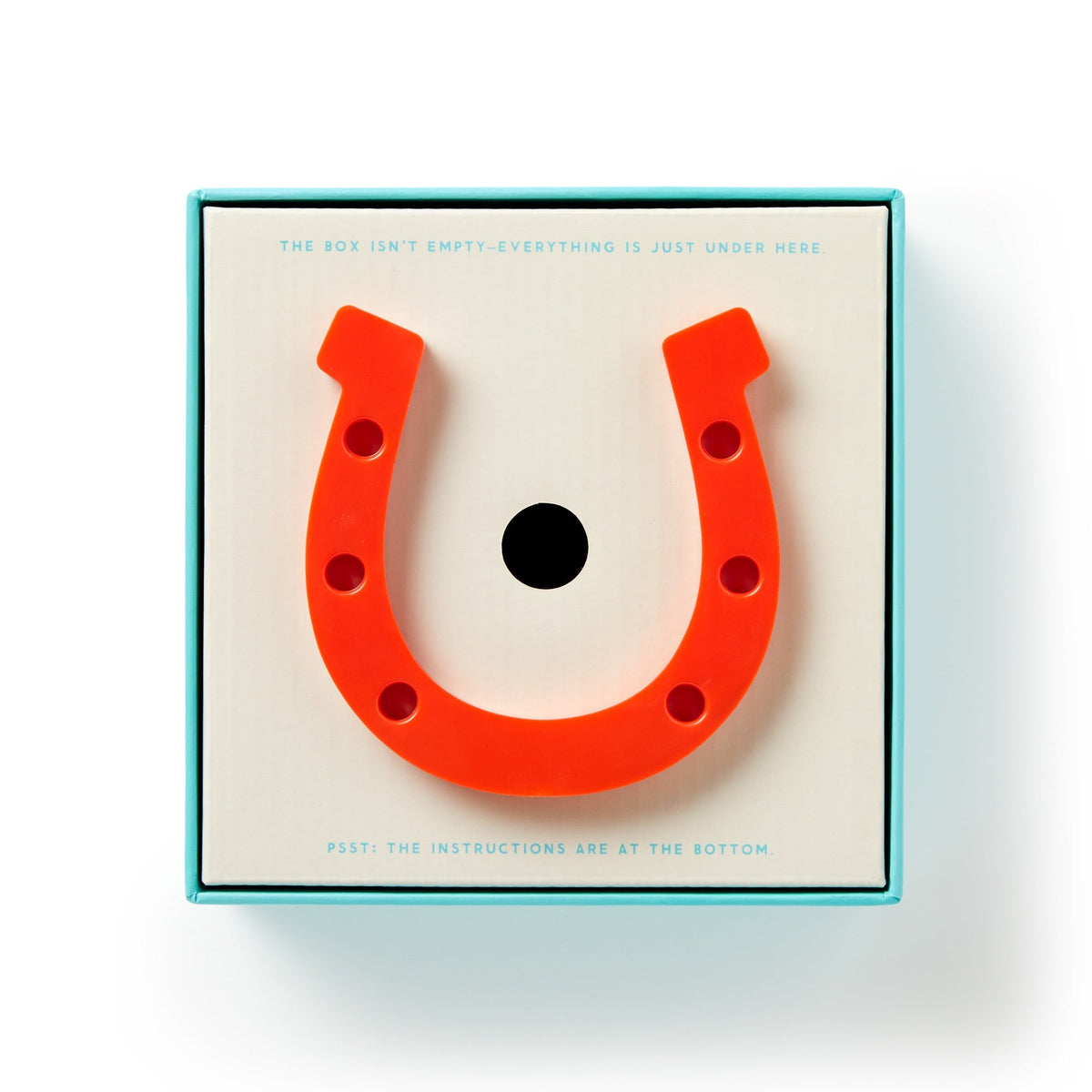 A bright red rubber horseshoe from the Brass Monkey Giddy Up Tabletop Horseshoes Game sits atop its box, which promises all game pieces and instructions are tucked inside—perfect for an indoor party match.