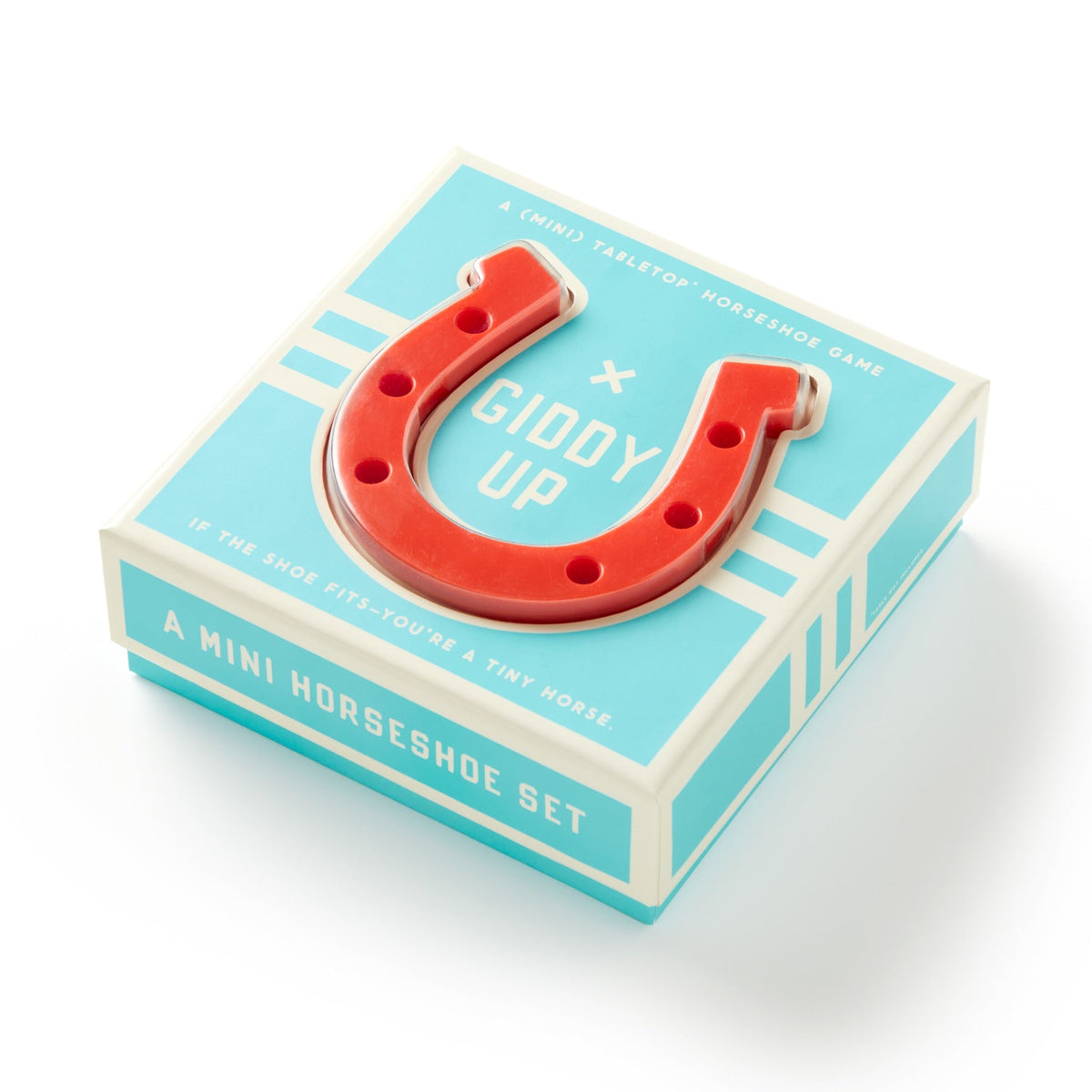 A blue and white Giddy Up Tabletop Horseshoes Game by Brass Monkey, featuring a red mini horseshoe on top. The box reads “A Mini Horseshoe Set—perfect as an indoor party game—and If the shoe fits—you’re a tiny horse.”.