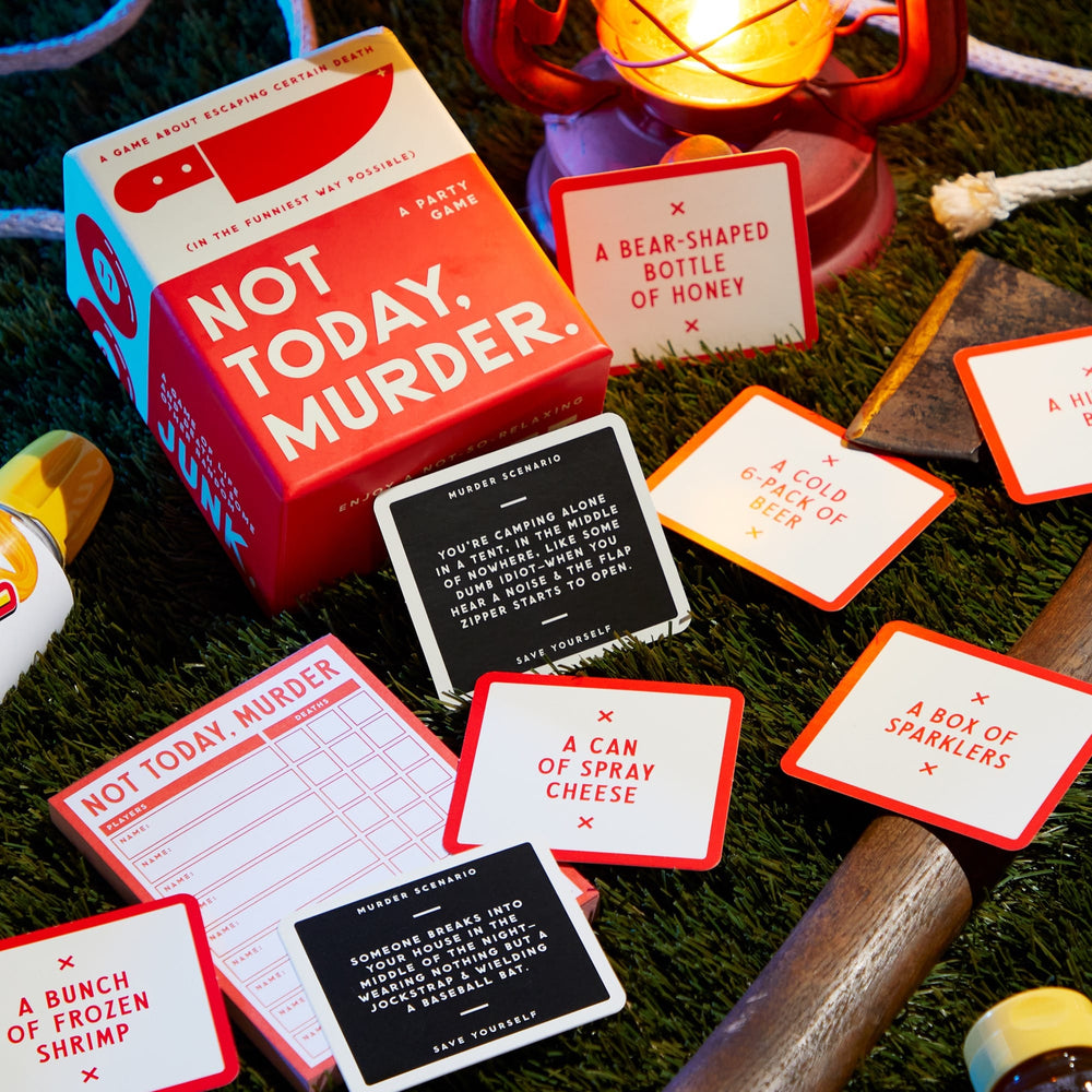 Not Today, Murder Game by Brass Monkey is a party game featuring game cards, a red lantern, a plastic yellow toy, and an axe on grass. Some cards list quirky items like a bear-shaped honey bottle for endless laughter in murder-y situations.