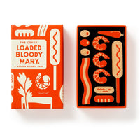 The (Over) Loaded Bloody Mary Balance Game by Brass Monkey is a boxed wooden game featuring cocktail garnish-shaped pieces like shrimp, olives, and bacon, neatly arranged in an open box.
