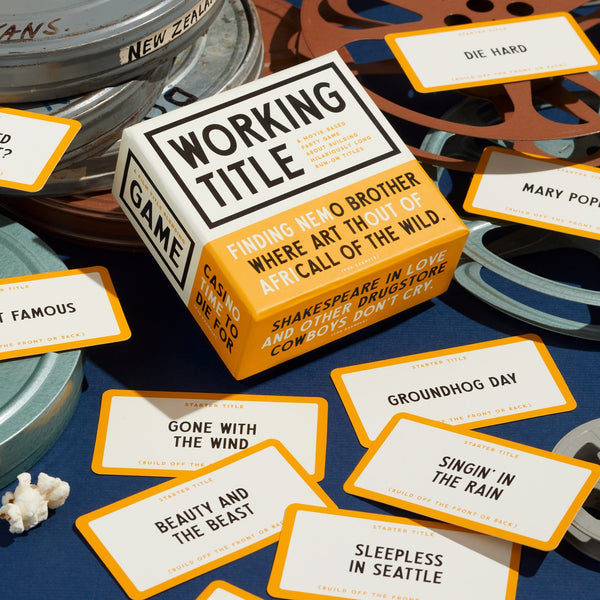 The Working Title Game by Brass Monkey is a boxed movie trivia game featuring film reel props and cards with famous movies like Die Hard, Groundhog Day, and Sleepless in Seattle.