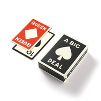 A Big Deal Giant Playing Cards by Brass Monkey are displayed on a white surface, featuring an oversized card with a spade and two red QUEEN cards with diamond symbols—all in a vintage-inspired design.