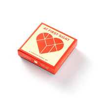 A red and cream box labeled At First Sight features an abstract heart design; inside is a unique tangram puzzle set from Brass Monkey.