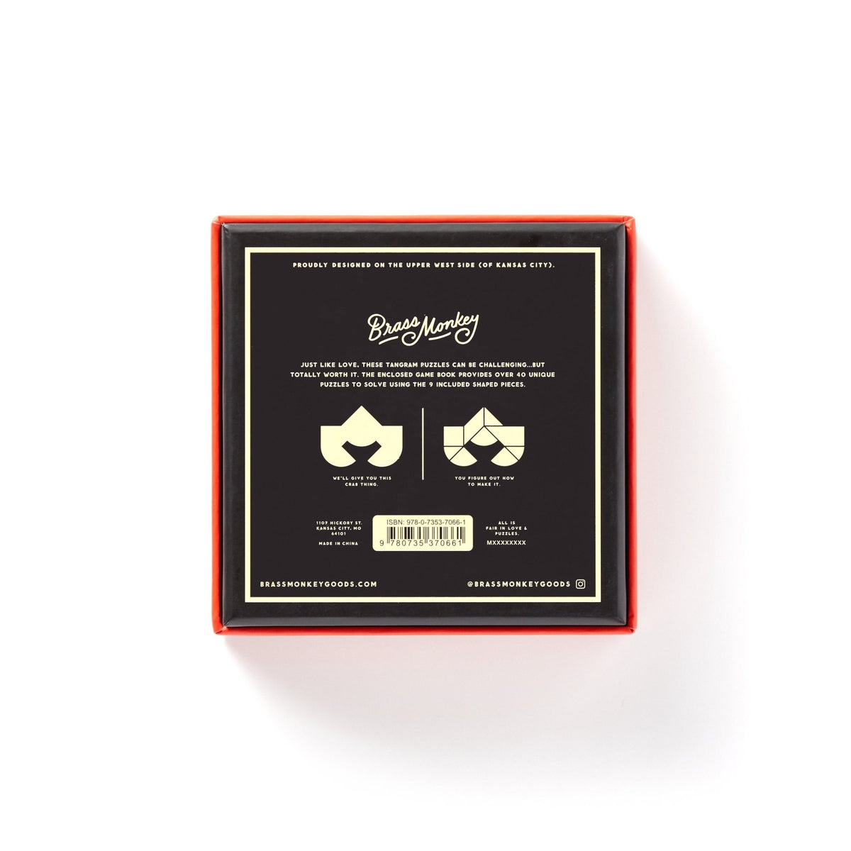 A square black box with orange edges, seen from above, labeled At First Sight Tangram Puzzle by Brass Monkey. The label highlights the challenge level and features unique puzzles plus two stylized faces with mustaches and sunglasses.