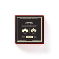 A square black box with orange edges, seen from above, labeled At First Sight Tangram Puzzle by Brass Monkey. The label highlights the challenge level and features unique puzzles plus two stylized faces with mustaches and sunglasses.