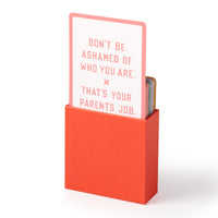 The Brass Monkey Emergency Affirmations for Exceptionally Stupid Days Card Deck comes in a red box; the visible card reads “DONT BE ASHAMED OF WHO YOU ARE. THATS YOUR PARENTS JOB.” in pink on white.