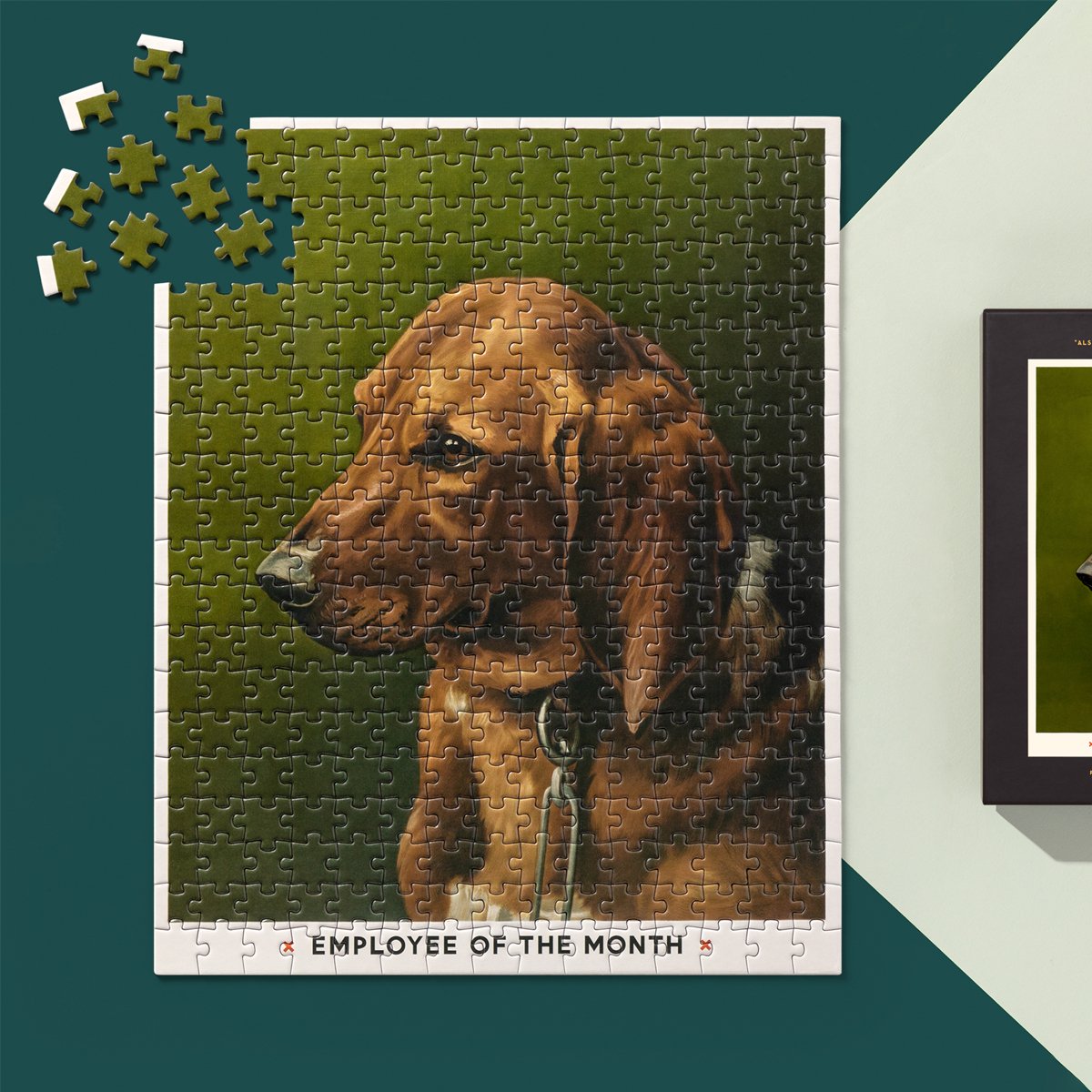 The Employee Of The Month 300 Piece Apartment Puzzle by Brass Monkey features a realistic brown dog with floppy ears. Loose pieces and part of the box are displayed nearby on a green surface, evoking classic vintage puzzles.