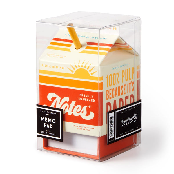 The Brass Monkey Freshly Squeezed Notes notepad block, shaped like a juice carton with a straw, features orange and yellow graphics, tear-off sheets, and the text Notes and 100% Pulp Because It’s Paper. Packaged in a clear plastic box.