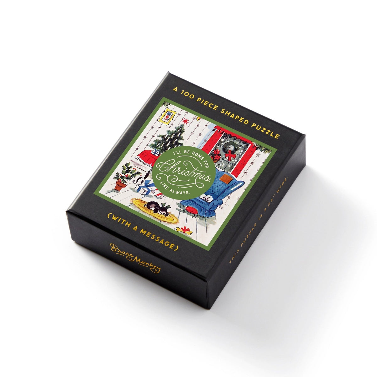 The Brass Monkey Home For Christmas 100 Piece Mini Shaped Puzzle comes in a black, giftable box featuring cozy Christmas living room art with a tree, gifts, and a cat. The box reads: Ill Be Home for Christmas, Always.