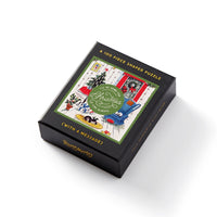 The Brass Monkey Home For Christmas 100 Piece Mini Shaped Puzzle comes in a black, giftable box featuring cozy Christmas living room art with a tree, gifts, and a cat. The box reads: Ill Be Home for Christmas, Always.