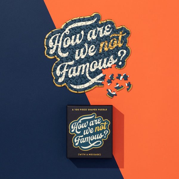 The Brass Monkey How Are We Not Famous? 100 Piece Mini Shaped Puzzle features the phrase on a blue and orange background, with scattered pieces and a matching giftable box displaying the same words.