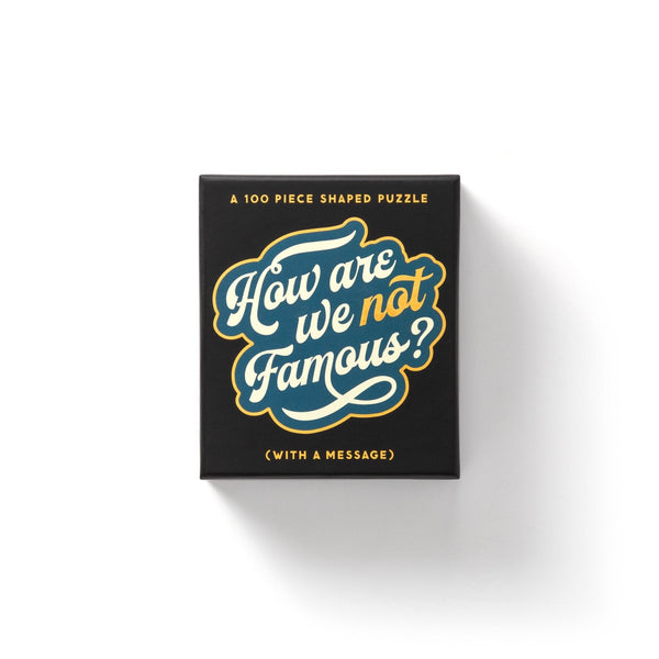 The Brass Monkey How Are We Not Famous? 100 Piece Mini Shaped Puzzle features bold, stylized text on a black box with giftable packaging, set against a white background.