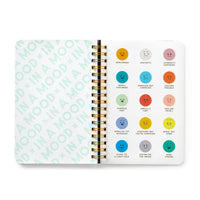 The Brass Monkey In A Mood Sticker Book is open, showing a mood chart with colorful emoticons and mood labels like bewildered, apathetic, smells a fart, and currently swooning. The left page repeats the green text: IN A MOOD.