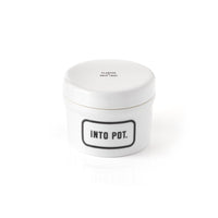 The Brass Monkey Into Pot Planter w/ Drip Tray is a white ceramic container with a fitted lid labeled INTO POT. in bold black, and small text PLASTER DRIP TRAY, featuring a vintage design against a plain white background.