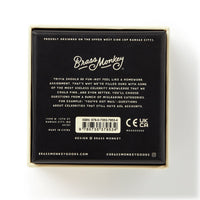 A sleek black box with white text presents Irrelevant Celebrity Trivia by Brass Monkey. The minimalist design highlights fun useless celeb facts, features contact info, an ISBN barcode, and certification logos.