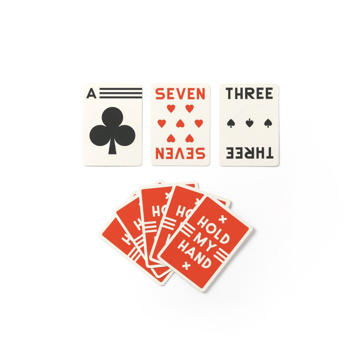 Three playing cards—ace of clubs, seven of hearts, and three of spades—are placed above five face-down red-back cards reading HOLD MY HAND in white. All cards are from the Brass Monkey Its In The Cards Playing Card Game Set.