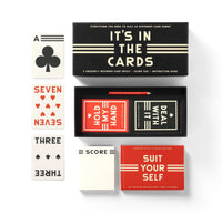 The Brass Monkey “It’s In The Cards Playing Card Game Set” includes two decks, a score pad, and instruction book. Shown with the ace of clubs, seven of hearts, and three of clubs alongside the box and accessories.