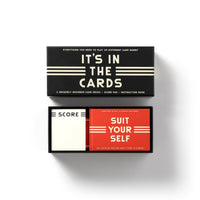 The Brass Monkey Its In The Cards Playing Card Game Set features two decks—Score and Suit Yourself—and an instruction book, all organized in a sleek black box with the lid off, perfect for card enthusiasts.
