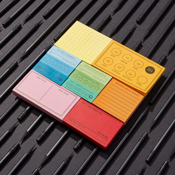 The Brass Monkey Ive Got A Few Notes Tear-off Notepad Set features colorful vintage-inspired designs and labels, arranged on a dark background with black pens placed diagonally.