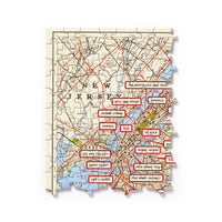 The Brass Monkey NYC Map 1,000 Piece Panoramic Puzzle features a vintage-style map of New Jersey and New York City with red labels marking iconic TV show locations like Friends, Seinfeld, Sesame Street, and more.