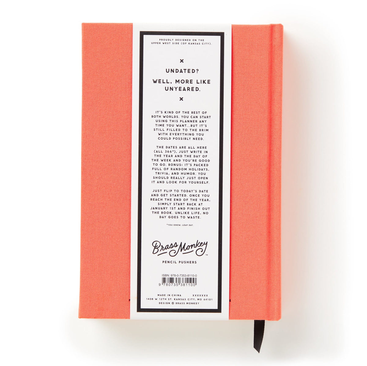The Part-Time Adult Undated Daily Planner by Brass Monkey features a coral hardcover, a white back label with playful undated text, barcode, and Brass Monkey logo. A black ribbon bookmark emerges from the bottom.