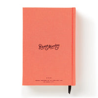 A coral pink hardcover Part-Time Adult Undated Daily Planner by Brass Monkey features black cursive branding and small text on the cover, plus a black ribbon bookmark. The planner is shown against a white background.