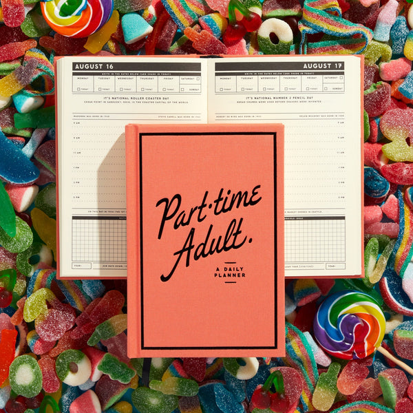 The Brass Monkey Part-Time Adult Undated Daily Planner, featuring a pink cover, rests on open planner pages surrounded by colorful gummy candies and lollipops.