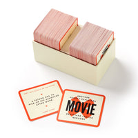 The Poorly Explained Movies Game by Brass Monkey features a cream box with two stacks of red-edged cards—ideal for parties. Displayed cards read: “A father has to pick up his daughter after work” and “MOVIE.”.