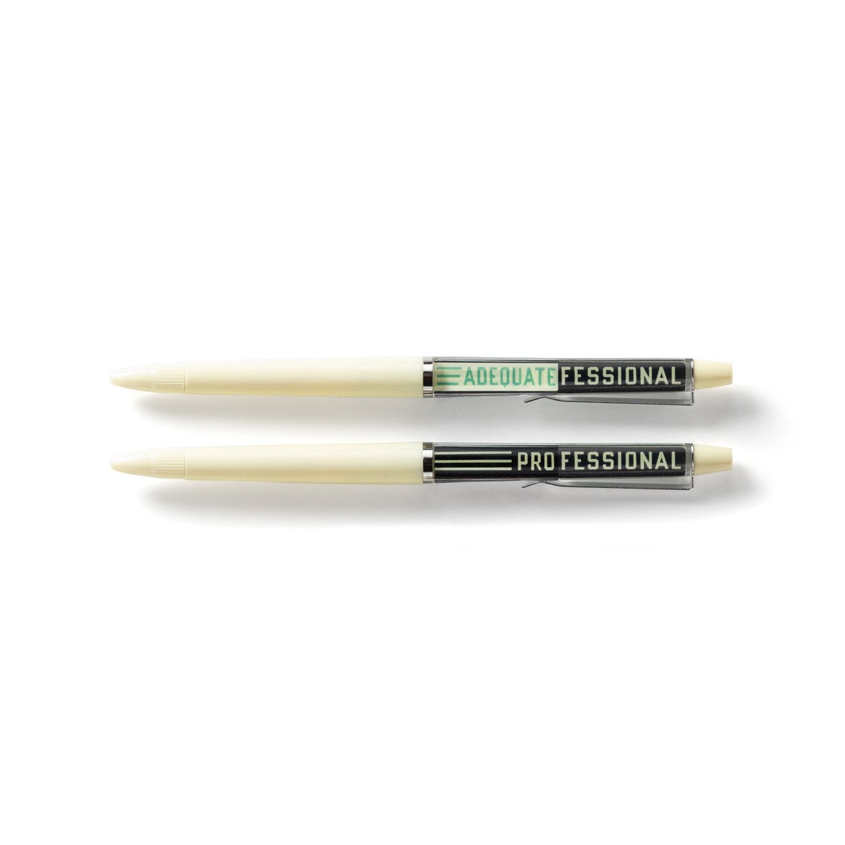 Two white, vintage-style floaty pens from Brass Monkey’s Professional Procrastinator Floaty Pen Set lie horizontally. One features ADEQUATE FESSIONAL in green; the other says PROFESSIONAL with “PRO” in white—both have black ink ballpoint tips.