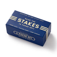 The Raise The Stakes Poker Game Set by Brass Monkey comes in a blue rectangular box with white and gold accents, featuring poker chips, a deck of cards, and a game booklet.