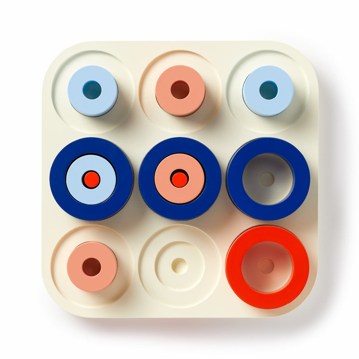 The Brass Monkey Tic Tac Pro Game Set features a square tray with nine circular recesses holding stackable painted wood pieces in blue, red, pink, and light blue—perfect for advanced tic-tac-toe or strategic play.