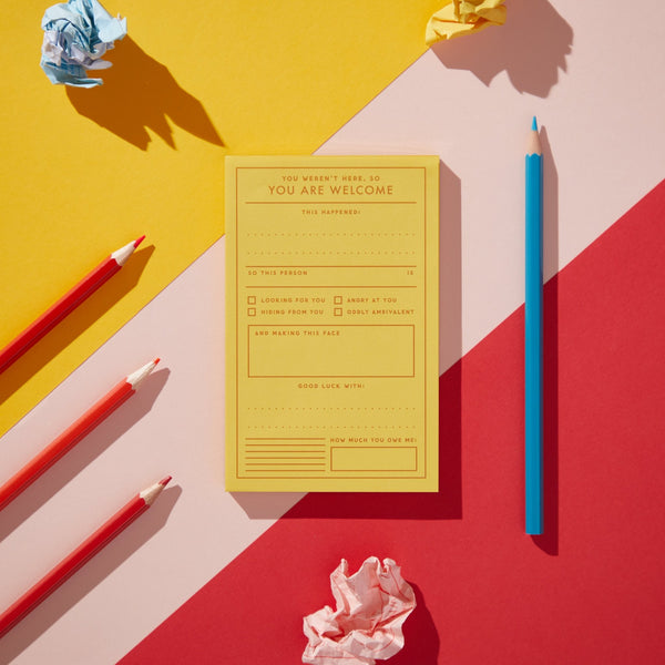 The You Are Welcome Memo Pad by Brass Monkey features checkboxes and prompts on a yellow card, set against a geometric yellow, red, and pink background with red and blue pencils—bringing vintage-inspired style to your workspace.