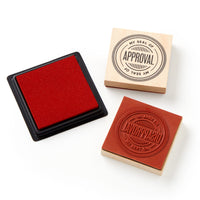 The Brass Monkey Your Seal Of Approval Stamp Set includes a red ink pad and two giant red stamps—one featuring the “MY SEAL OF APPROVAL” design and the other showing its raised rubber side.