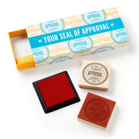 The Brass Monkey Your Seal Of Approval Stamp Set includes a box with two wooden stamps—one upright, one face down—featuring the circular Seal of Approval design, plus a large color inkpad.