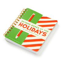 The Brass Monkey Beyond Bored At The Holidays is a spiral-bound book with a green and red striped cover, an illustrated pencil, and fun adult activities.