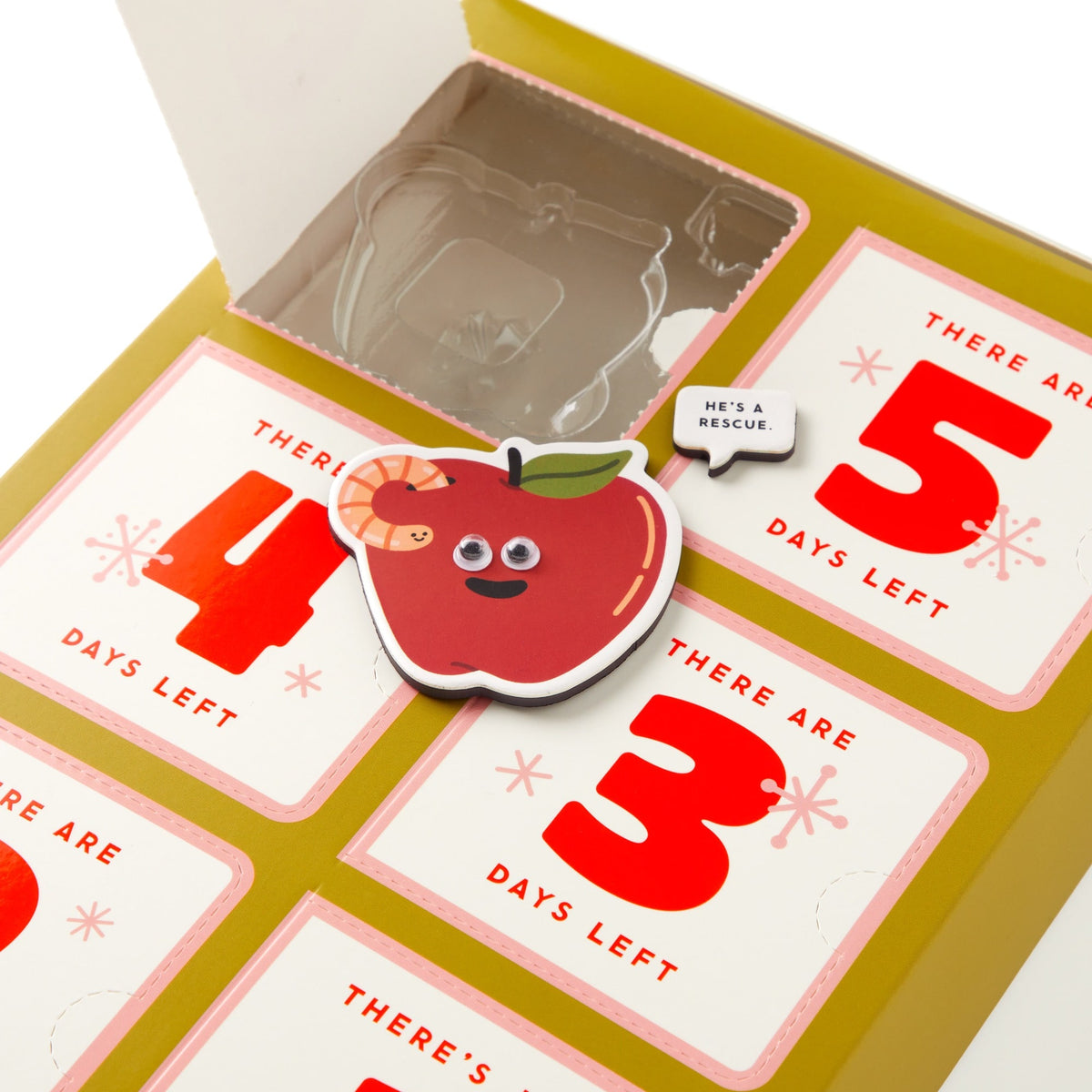 The Brass Monkey Oh What Googly-Eyed Fun Magnet Countdown Calendar features a cute apple-shaped magnet with googly eyes and a worm beside a “He’s a rescue” speech bubble, counting down the days in bold red numbers.