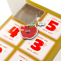 The Brass Monkey Oh What Googly-Eyed Fun Magnet Countdown Calendar features a cute apple-shaped magnet with googly eyes and a worm beside a “He’s a rescue” speech bubble, counting down the days in bold red numbers.