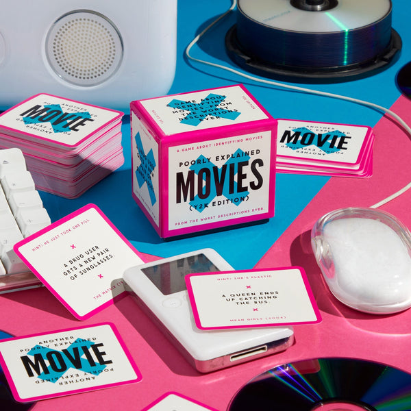 A colorful tabletop scene showcases Brass Monkey’s Mini Poorly Explained Movies – Y2K Edition, with playful movie description cards, a pink-edged box, a computer mouse, CDs, and a speaker on a blue and pink background.