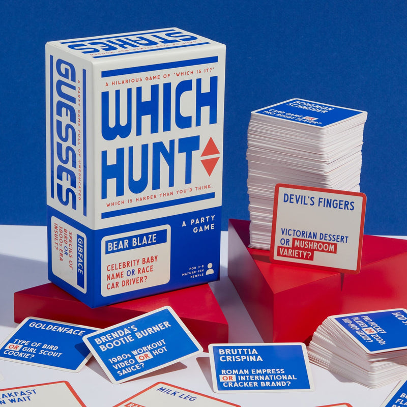 The Which Hunt Party Game by Brass Monkey, an adult trivia card game in blue and white packaging, sits on a table with red stands holding stacks of cards. Some playful question cards are spread out in front.