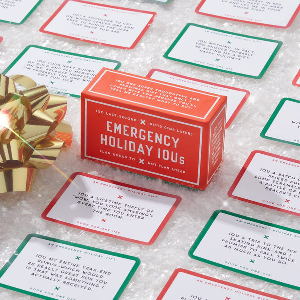 The Brass Monkey Emergency Holiday IOUs Card Set sits on a sparkly white surface, surrounded by colorful cards and a gold gift bow. Each card offers thoughtful gifts like chores, a movie marathon, or snacks.