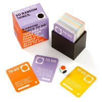The Brass Monkey Random Things To Do Box is a boxed card game set featuring colorful TO DO cards, a six-sided die, and an orange box. Three sample cards and the die are shown in front of the box labeled "RANDOM THINGS TO DO.