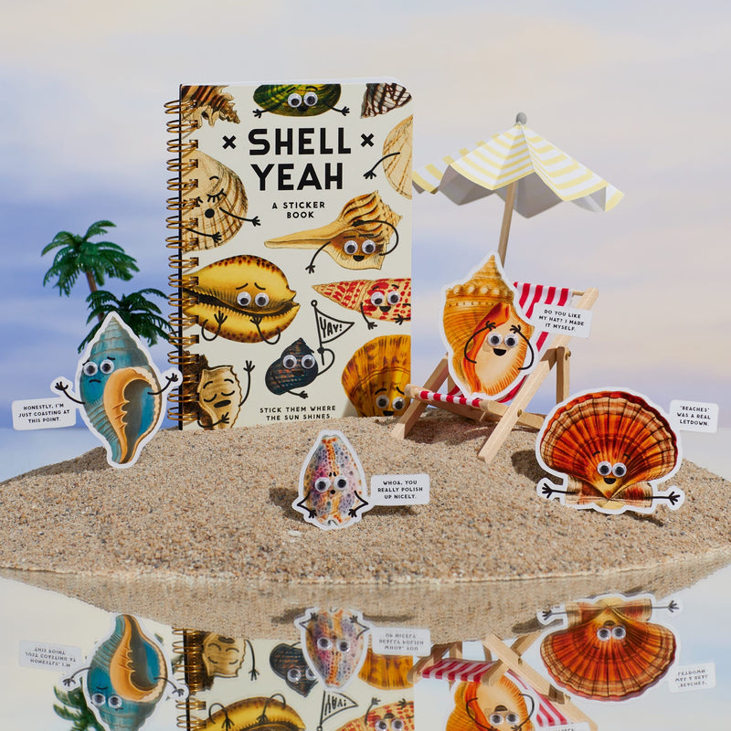 The Brass Monkey Shell Yeah Sticker Book sits on sand, surrounded by adorable seashell stickers with googly eyes, a beach umbrella, and playful speech bubbles—all reflected on a shiny surface beneath a blue sky with clouds.