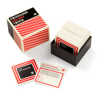 A box of Brass Monkey’s Frivolous Holiday Trivia is pictured with the lid off, revealing a stack of cards in a black tray and two displayed cards, one featuring a question about The Nutcracker.