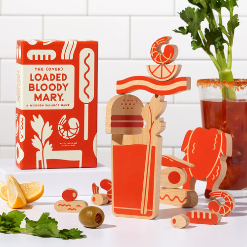 The (Over) Loaded Bloody Mary Balance Game by Brass Monkey features wooden pieces shaped like celery, lemon, and more. Assembled beside its red and white box, it's the perfect party game for your next brunch!.